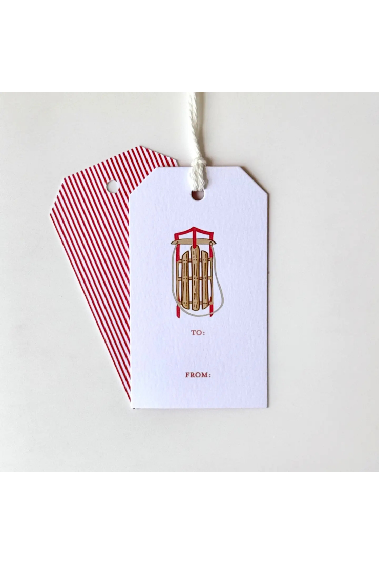 A white gift tag with a red and white striped backer card, featuring a small illustration of a snowmobile and the text 'TO:' and 'FROM:' on a light gray background.