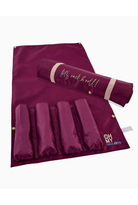 A burgundy nylon hair roll organizer with five vertical pockets, shown partially unrolled with a matching rolled-up section resting across the top. The top section features the text 'let's rock 'roll!!' in white script, and the bottom right corner displays a gold and blue 'MHW MARY HAWKS' logo.