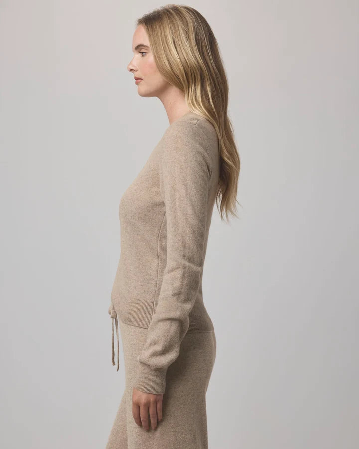 A woman in side profile wearing a light beige knit sweater and matching knit skirt against a plain light gray studio background.