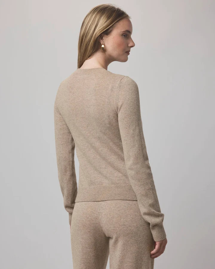 A woman shown from the back wearing a light beige knit sweater and matching knit pants against a plain light gray studio background.