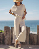 Woman in a white outfit standing by the ocean with wooden posts in the foreground