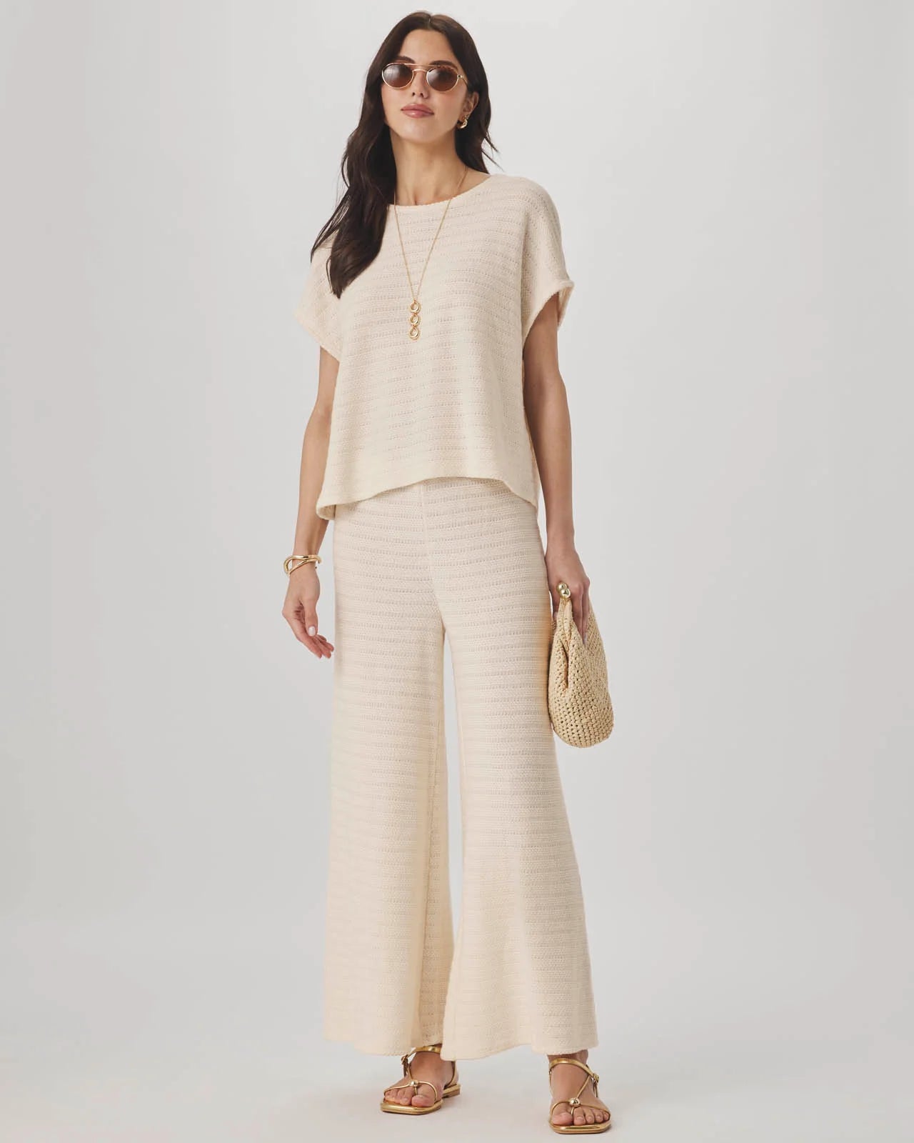 Woman wearing a beige outfit with wide-leg pants and sandals on a white background