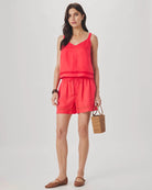 Woman wearing a coral sleeveless top and shorts set, holding a woven bag on a white background