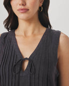 Woman wearing a dark sleeveless top with a V-neckline on a plain background