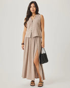 Woman wearing a sleeveless beige top and long skirt with a black handbag on a white background