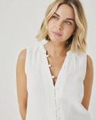 Woman wearing a white sleeveless top with buttons on a plain background