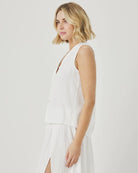 Woman wearing a white sleeveless dress against a plain background