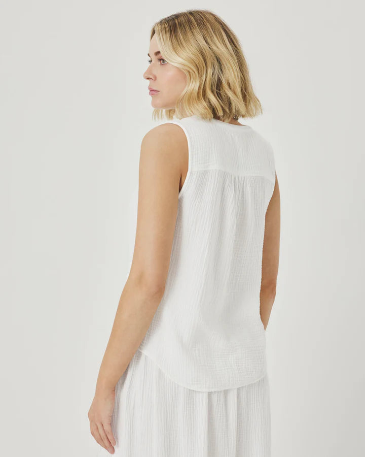 Woman wearing a white sleeveless top with pleated skirt on a light gray background