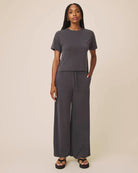 Woman wearing a gray outfit with wide-leg pants on a beige background