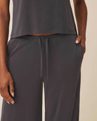 Person wearing a dark gray sleeveless top and wide-leg pants on a beige background