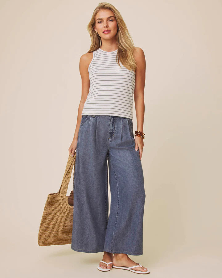 Woman wearing a striped tank top and wide-leg jeans, holding a straw bag on a beige background