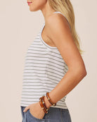 Woman wearing a striped tank top and denim shorts with wooden bracelets on a beige background