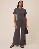 Woman wearing a gray outfit with wide-leg pants on a beige background