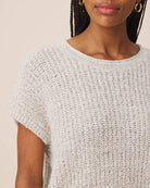 Close-up of a woman wearing a short-sleeve knit top in a light heathered off-white color, showing the textured waffle knit fabric and crew neckline.