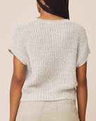 A person shown from the back wearing a short-sleeve textured knit top in a light heather gray color, paired with light beige pants, against a solid light beige background.