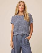 Woman wearing a blue textured top and denim pants against a beige background