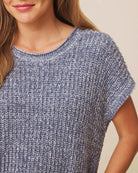 Close-up of a woman wearing a short-sleeve knit top in a heathered blue-gray color, showing the ribbed texture and crew neckline.