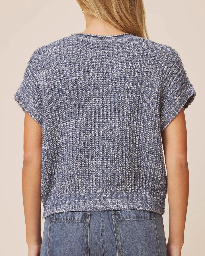 A person shown from the back wearing a short-sleeve textured knit top in a heathered blue-gray color, paired with blue jeans against a plain beige studio background.