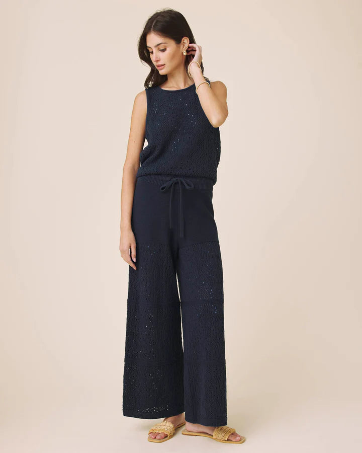 Woman wearing a navy blue sleeveless top and wide-leg pants on a beige background
