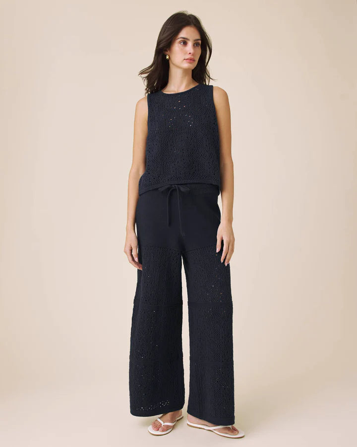 Woman wearing a navy sleeveless top and wide-leg pants on a beige background