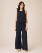 Woman wearing a navy sleeveless top and wide-leg pants on a beige background