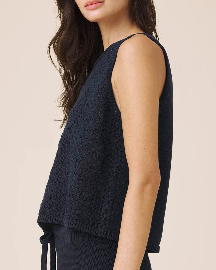 Woman wearing a dark blue sleeveless knitted top against a beige background