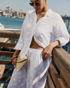 Woman in white outfit standing by a waterfront with sunglasses on