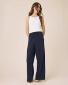 Woman wearing navy wide-leg pants and a white top on a beige background