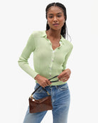 A woman modeling a light green ribbed knit button-up cardigan with a collar, paired with blue jeans and holding a small brown handbag, against a plain white background.
