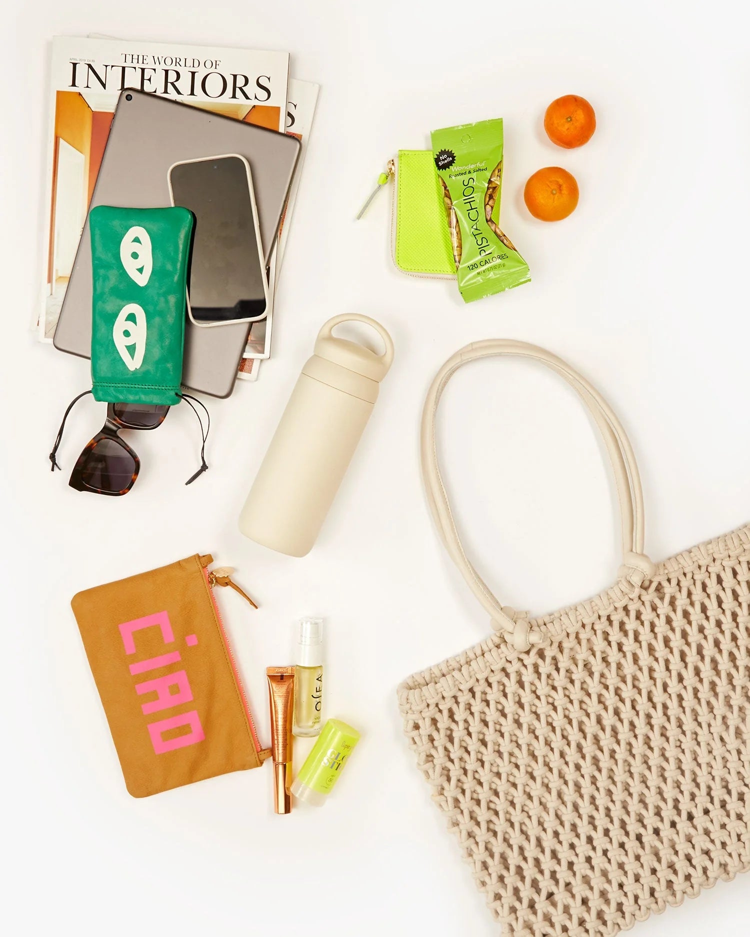 Beige woven bag with travel items including a water bottle, phone, and snacks on a white background