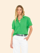 Woman wearing a green shirt and white pants on a beige background