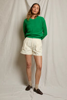 Woman wearing a green sweater and white shorts against a plain background