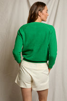 Person wearing a green sweater and white shorts against a plain background