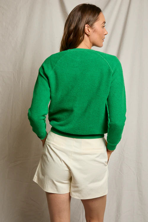 Person wearing a green sweater and white shorts against a plain background