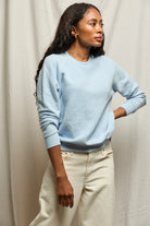 Woman wearing a light blue sweater and beige pants against a neutral background