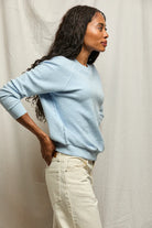 Woman wearing a light blue sweater and beige pants against a neutral background