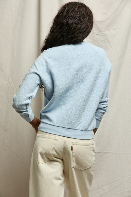 Person wearing a light blue sweater and beige pants against a plain background