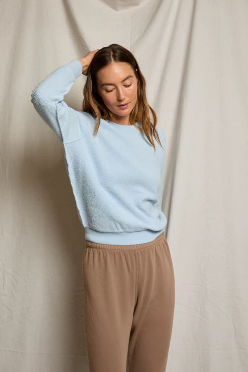 Woman wearing a light blue sweater and beige pants against a neutral background
