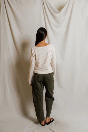 Person wearing a white sweater and green pants standing against a plain white curtain.