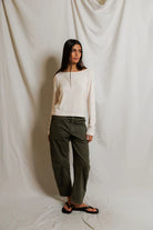 Woman wearing a white sweater and green pants against a plain background