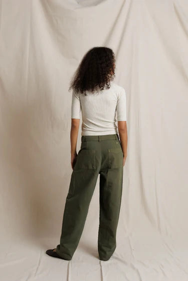 Person wearing a white top and green pants standing against a plain background