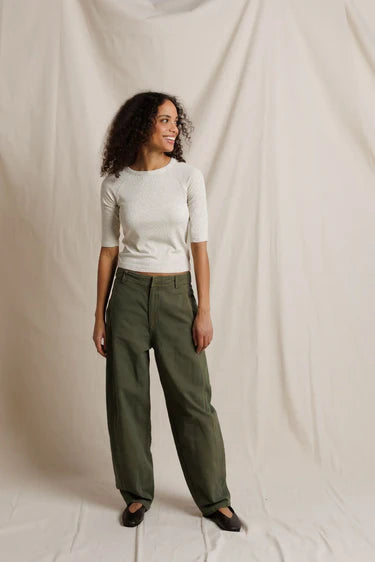 Woman wearing a white top and green pants against a beige background