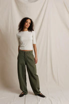 Woman wearing a white top and green pants against a plain background