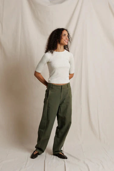 Woman wearing a white top and green pants against a plain background