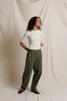 Woman wearing a white top and green pants against a plain background