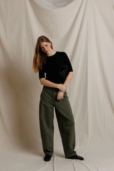 Person wearing a black top and green pants against a beige backdrop