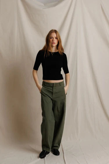 Woman wearing a black top and green pants against a plain background