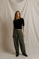Woman wearing a black top and green pants against a plain background