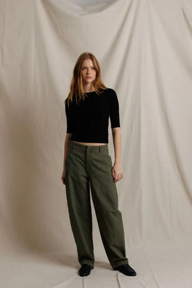 Woman wearing a black top and green pants against a plain background