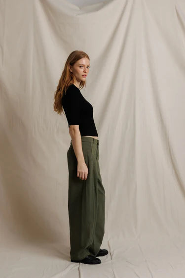 Woman wearing a black top and green pants against a plain background